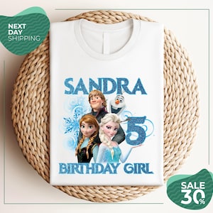 A white t-shirt with a design featuring characters from the Disney movie Frozen, specifically Elsa, Olaf, and Anna, along with the text "SANDRA BIRTHDAY GIRL".