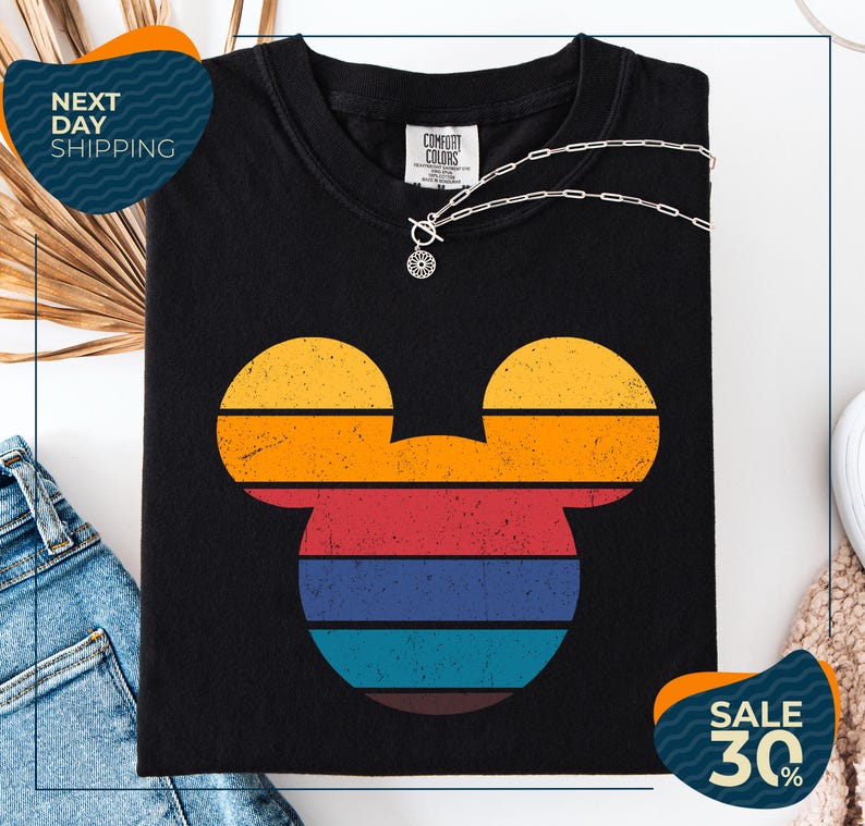 a black t-shirt with a colorful Mickey Mouse design, along with a pair of jeans and a necklace. The t-shirt is displayed on a white background, and there are two sale signs indicating a 30% discount.