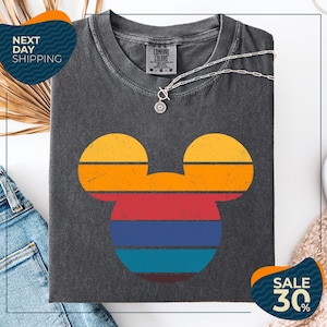 a gray t-shirt with a colorful Mickey Mouse design, along with a pair of jeans and a beige sweater. The t-shirt is displayed on a white background, and there are two sale signs indicating a 30% discount.