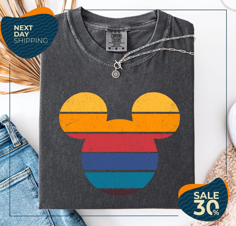 a gray t-shirt with a colorful Mickey Mouse design, along with a pair of jeans and a beige sweater. The t-shirt is displayed on a white background, and there are two sale signs indicating a 30% discount.
