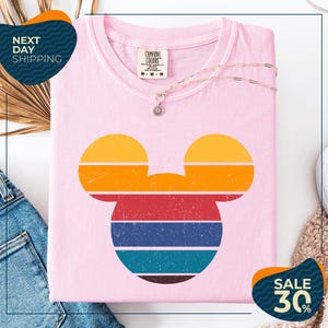 a pink t-shirt with a colorful Mickey Mouse design, along with a pair of jeans and a necklace. The t-shirt is displayed on a white background, and there are two sale signs indicating a 30% discount.