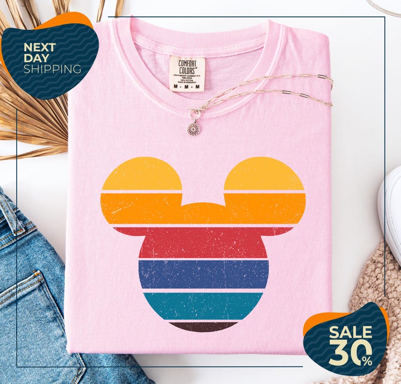 a pink t-shirt with a colorful Mickey Mouse design, along with a pair of jeans and a necklace. The t-shirt is displayed on a white background, and there are two sale signs indicating a 30% discount.
