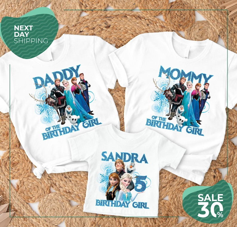 three white t-shirts with the same design, each with a different character from the Disney movie Frozen. The design includes the characters Elsa, Anna, Olaf, and other popular characters from the movie. The t-shirts are arranged on a bed of straw, and there is a sale sign indicating a 30% discount on the t-shirts.