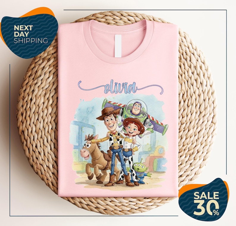 A pink t-shirt featuring characters from the Toy Story movie, including Woody, Buzz Lightyear, and a girl, along with a horse and a dog.