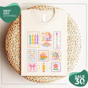 a white t-shirt with a colorful graphic design, including various school-related items such as crayons, a paint palette, a backpack, and a pencil. The t-shirt is displayed on a woven basket, and there are two green circular signs in the background that read "Next Day Shipping" and "SALE 30%".