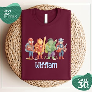 A burgundy t-shirt with a colorful graphic design featuring four superhero characters, including Spider-Man, Iron Man, Captain America, and Wiliam.