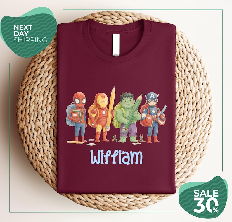 A burgundy t-shirt with a colorful graphic design featuring four superhero characters, including Spider-Man, Iron Man, Captain America, and Wiliam.