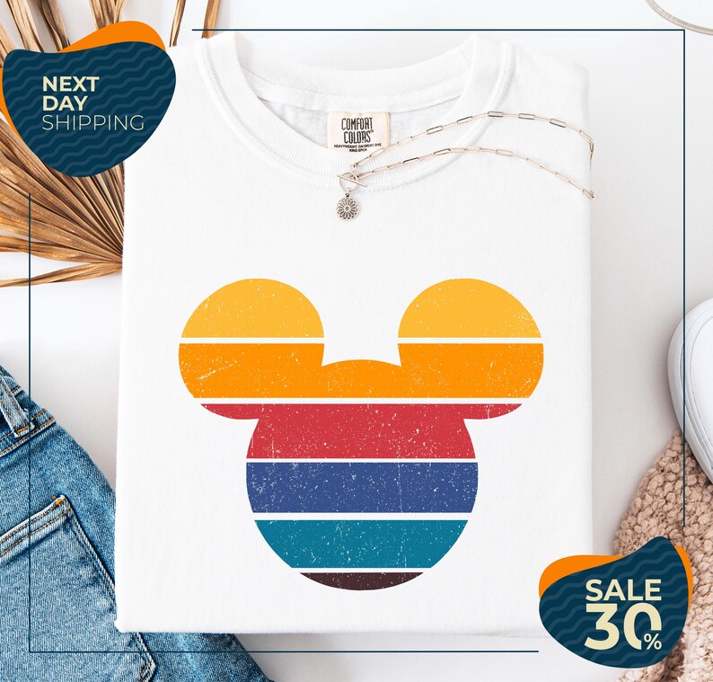 a white t-shirt with a colorful Mickey Mouse design, along with a pair of jeans and a necklace. The t-shirt is displayed on a white background, and there are two sale signs indicating a 30% discount.