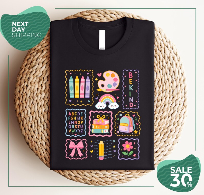 a black t-shirt with a colorful and whimsical design, including various school-related items such as pencils, books, and a backpack, along with the text "BEKIND" and "SALE 30%".