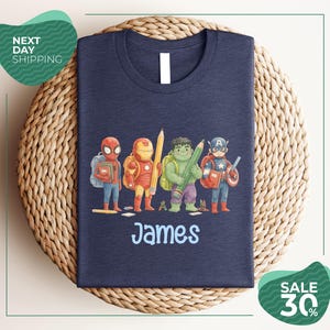 A navy blue t-shirt with a graphic design featuring four cartoon characters, including Spider-Man, Iron Man, Captain America, and James, standing together.