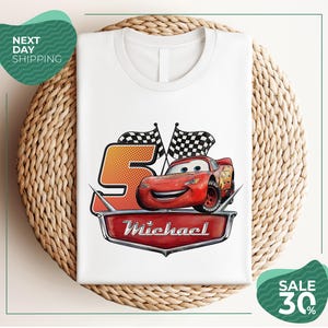 A white t-shirt with a graphic design featuring a red car and checkered flags, along with the text "Michael" and "Sale 30%".