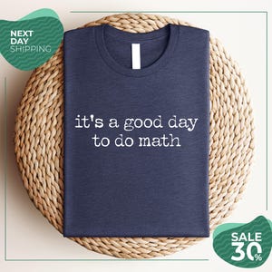 May include: A dark navy blue short-sleeved t-shirt featuring the white text "it's a good day to do math" printed in a typewriter-style font across the center of the chest. The shirt has a classic crew neckline and a simple, clean design.