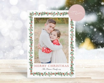 May include: A Christmas card featuring a photo of two children hugging, framed by a border of green holly leaves and red berries. The words "MERRY CHRISTMAS" and family name are printed in red at the bottom.