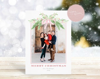 May include: A Christmas card featuring a family portrait inside a red border. The card is decorated with watercolor greenery and a pink bow. The words "MERRY CHRISTMAS" are printed in red, along with the family's name and the year 2022.