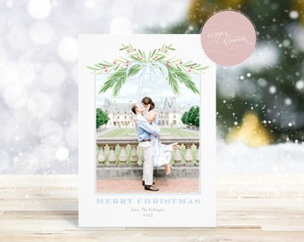 May include: A Christmas card featuring a couple embracing in front of a stately building. The card has a watercolor design with greenery and berries at the top, a blue border, and the text "MERRY CHRISTMAS" and "Love, The Dellingers 2023".