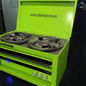 May include: A white ceramic mug with a black handle and the text "But First, Coffee" in a bold, black font. The mug is set against a blurred background, suggesting a cozy setting.