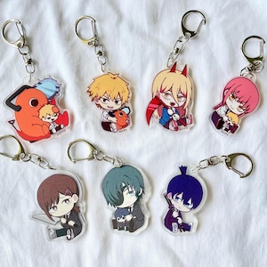 Könnte beinhalten: Sammlung von sieben Anime-Schlüsselanhängern mit farbenfrohen Charakterdesigns. Jeder Schlüsselanhänger hat einen silberfarbenen Metallring und -verschluss. Die Charaktere haben unterschiedliche Haarfarben und Outfits. Die Schlüsselanhänger sind aus klarem Acryl gefertigt.