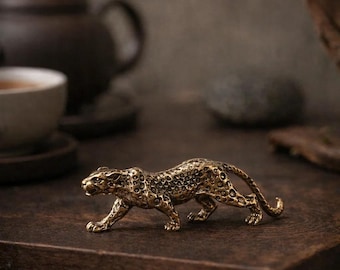 May include: A detailed, golden-colored leopard figurine. The sculpture is posed in a walking stance, with intricate detailing on its spotted coat. The figurine is placed on a dark wooden surface, suggesting a decorative item.