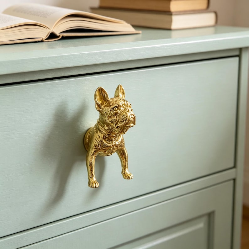 Peut inclure: Un bouton de tiroir en m&eacute;tal dor&eacute; en forme de bouledogue fran&ccedil;ais. Le bouton pr&eacute;sente une sculpture tridimensionnelle d&eacute;taill&eacute;e de la t&ecirc;te, du poitrail et des pattes avant du chien, fix&eacute;e sur une fa&ccedil;ade de tiroir en bois peint en vert clair.