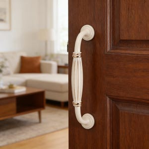 Op de afbeelding: Een crèmekleurige deurklink met een gecanneleerd middengedeelte en metallic goudkleurige accenten aan de boven- en onderkant, verticaal gemonteerd op een donkerbruine houten deur met paneelontwerp en ronde basisplaten aan beide uiteinden.
