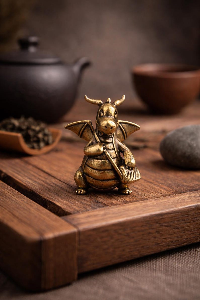 May include: A detailed brass dragon figurine with wings, horns, and a small bag. The dragon is posed on a wooden surface, suggesting a decorative or collectible item. The dragon is a golden color.