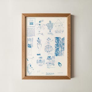 May include: A framed print with blue sketches of figures and clothing designs on a cream background. The print includes the word "ROBE" in blue text. The frame is made of light brown wood.