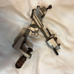 Peut inclure: Un outil métallique vintage de couleur argentée, avec des bras réglables et une poignée en bois. L'outil comporte plusieurs boulons et vis, ce qui suggère qu'il est conçu pour des ajustements ou des mesures précis. L'outil est probablement utilisé à des fins mécaniques ou d'ingénierie.