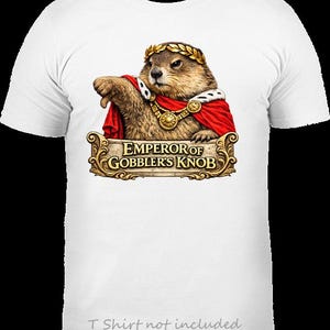 May include: White t-shirt featuring a groundhog wearing a gold laurel wreath and a red cape. The groundhog is depicted with a regal expression, and the text "EMPEROR OF GOBBLER'S KNOB" is displayed below. The shirt's design is centered.