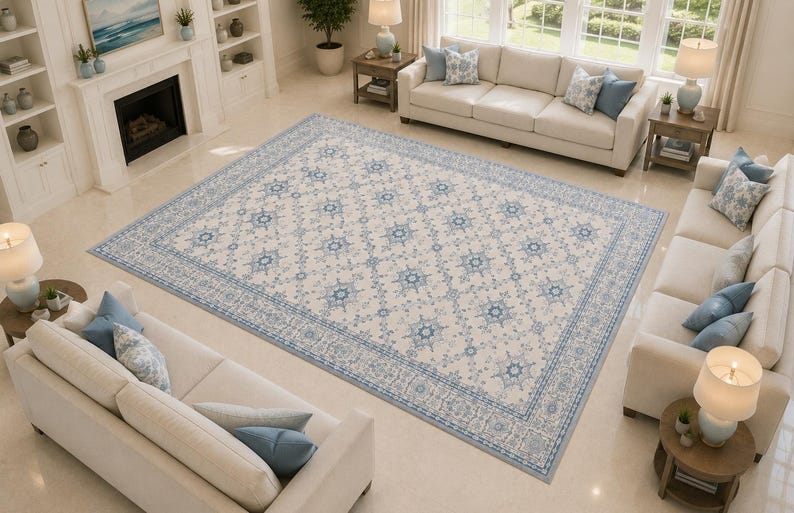K&ouml;nnte beinhalten: Ein gro&szlig;er rechteckiger Teppich mit cremefarbener Basis, verziert mit einem sich wiederholenden Muster aus blauen Blumenmedaillons und komplexen geometrischen Bord&uuml;ren. Der Teppich liegt mittig in einem Wohnraum mit hellem Boden.