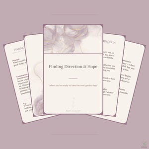 May include: A deck of cards with a light purple and white marbled design featuring gold accents. The central card displays the text Finding Direction & Hope, when you're ready to take the next gentle step, and the brand name Eden's Corner.