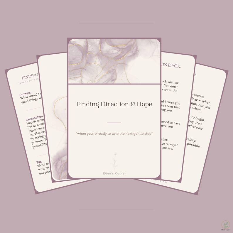 May include: A deck of cards with a light purple and white marbled design featuring gold accents. The central card displays the text Finding Direction & Hope, when you're ready to take the next gentle step, and the brand name Eden's Corner.