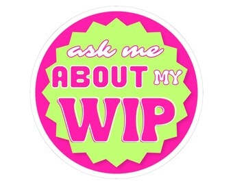 May include: A round sticker with a pink border and a lime green starburst design in the center. The sticker has the text "ask me about my WIP" in white and pink lettering.
