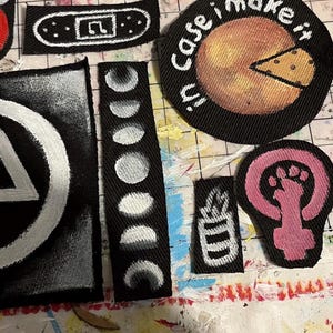 May include: A selection of handmade fabric patches with diverse designs. Includes a patch with a circle and a triangle, a pizza slice, and patches with the phrases "Punk's not dead" and "Eat the rich".