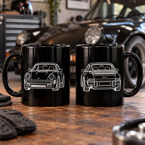 May include: Two black ceramic mugs featuring white line art illustrations of a sports car. The left mug displays the front view of the vehicle, while the right mug shows the rear view with the word turbo printed on the back of the car.