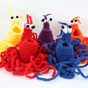 May include: Five crocheted octopus plushies in different colors: yellow, red, purple, blue, and orange. Each octopus has large white eyes and a crocheted body with long tentacles.