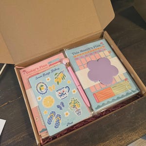 Op de afbeelding: Een briefpapier geschenkdoos met een roze Today's Plan notitieblok, een blauw Lemon Breeze stickervel, een lichtblauw This Month's Plan kalenderblok, een roze pen met een ronde dop en een paars, bloemvormig memoblaadje.