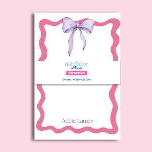 May include: A white notepad featuring a light purple watercolor bow at the top and a pink wavy border. A central band displays the text The Saltwater Press, NOTEPAD, and SHOPSALTWATERPRESS.COM. The name Addie Lamar is printed at the bottom.
