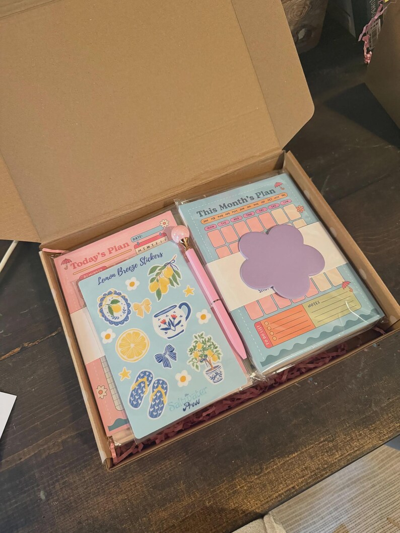 Puede incluir: Una caja de regalo con art&iacute;culos de papeler&iacute;a. Incluye un planificador, pegatinas, un bol&iacute;grafo y un bloc de notas. Las pegatinas tienen un tema de lim&oacute;n. El planificador y el bloc de notas tienen una combinaci&oacute;n de colores pastel con una nota adhesiva en forma de flor.