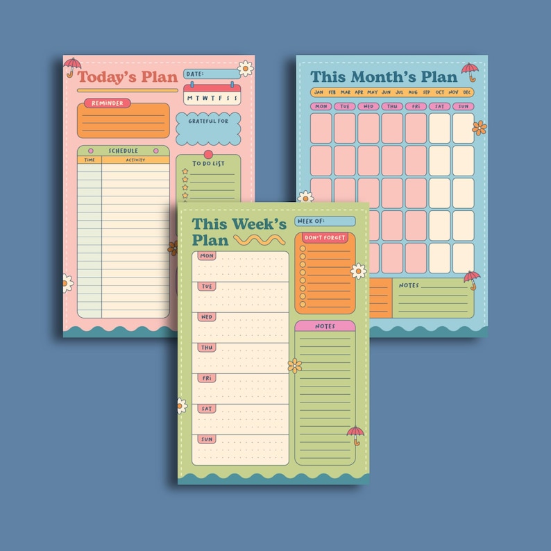 Op de afbeelding: Drie rechthoekige papieren planners met de titels Today's Plan in roze, This Month's Plan in blauw en This Week's Plan in groen. Elk vel bevat secties voor schema's, takenlijsten en notities, versierd met kleine bloem- en paraplu-iconen.