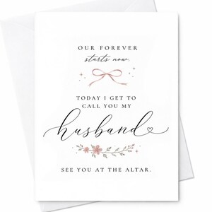 May include: A white greeting card featuring black text that reads: OUR FOREVER starts now. TODAY I GET TO CALL YOU MY husband. SEE YOU AT THE ALTAR. The design includes a small pink bow, decorative sparkles, and a floral vine with pink flowers.