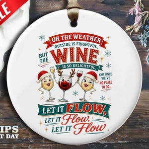 May include: A round white ceramic ornament with a brown ribbon hanger. The design features three anthropomorphic wine glasses with faces, two wearing Santa hats and one with reindeer antlers. Text reads: Oh the weather outside is frightful, but the wine is so delightful, and since we've no place to go, let it flow, let it flow, let it flow.
