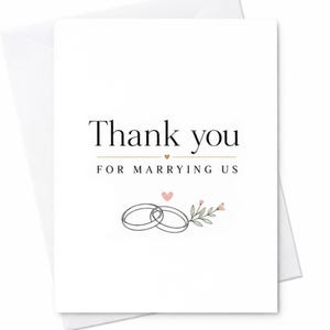 May include: A white greeting card with the black text Thank you FOR MARRYING US. The design features a small gold heart, a pink heart, and a line drawing of two interlocking rings decorated with a small sprig of green leaves and pink flowers.
