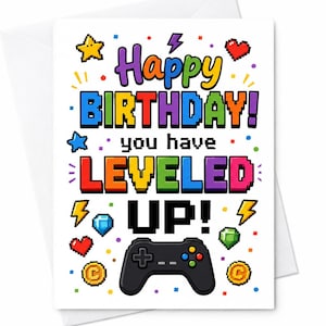 May include: A white greeting card featuring colourful pixelated text that reads Happy BIRTHDAY! you have LEVELED UP! The design includes a black game controller, a yellow star, a red heart, a blue diamond, a green gem, and two gold coins.