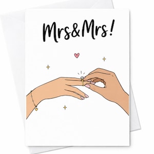 May include: A white greeting card featuring the black text Mrs & Mrs! above an illustration of two hands. One hand wears a gold ring with a diamond and a delicate gold bracelet with a heart charm. Small pink hearts and yellow stars decorate the card.