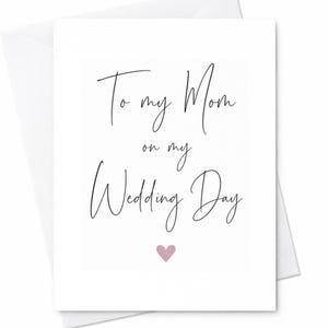 May include: A white greeting card with black cursive text that reads To my Mom on my Wedding Day. Below the text is a small, solid, light pink heart. The card is positioned on top of a matching white envelope, creating a clean and simple design.