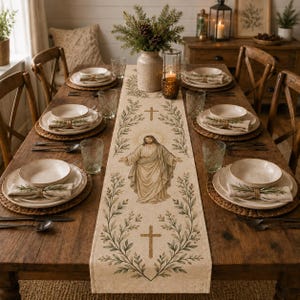 May include: A beige fabric table runner featuring a central illustration of Jesus with arms outstretched, surrounded by green leafy branches and two crosses. The runner is displayed on a wooden dining table set with white bowls and napkins.