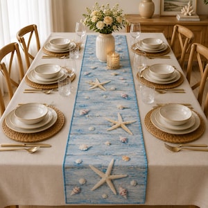 May include: A dining table set for four with a beige tablecloth and a blue wooden-plank patterned table runner featuring starfish and seashell prints. The setting includes woven placemats, white ceramic bowls, plates, glassware, and silverware.