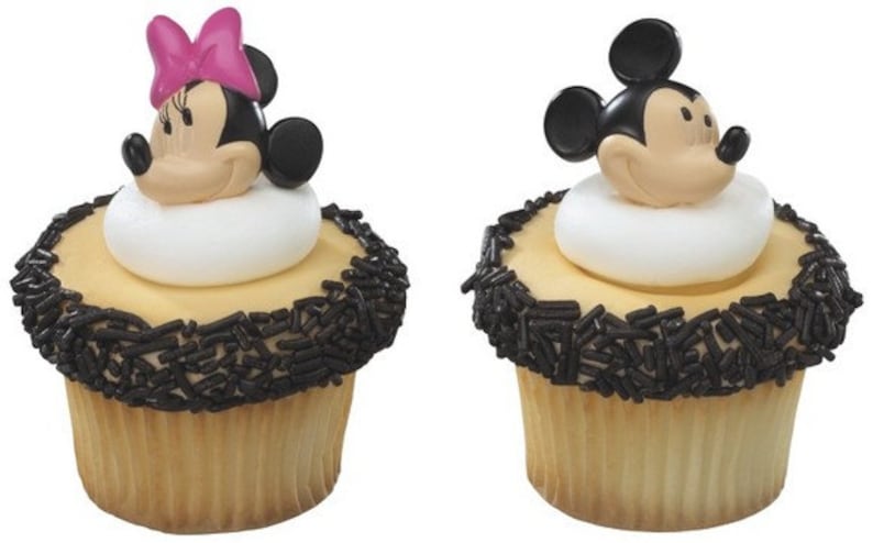 May include: Two cupcakes decorated with black sprinkles and fondant Mickey Mouse and Minnie Mouse toppers.