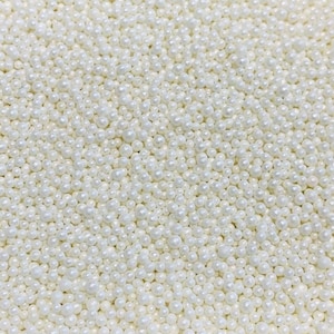 Puede incluir: Una imagen de primer plano de espolvorear perlas blancas. Las chispas son pequeñas y redondas, y son perfectas para decorar pasteles, cupcakes y otros postres.