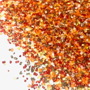 May include: A close-up of a variety of colorful sprinkles, including red, orange, yellow, and brown. The sprinkles are small and rectangular in shape.
